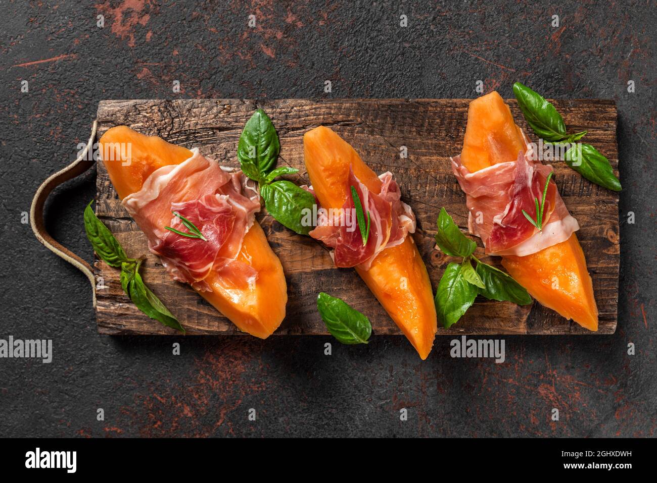 Fette di melone cantalupo con prosciutto e basilico su sfondo nero. Antipasto italiano. Vista dall'alto. Cibo sano Foto Stock