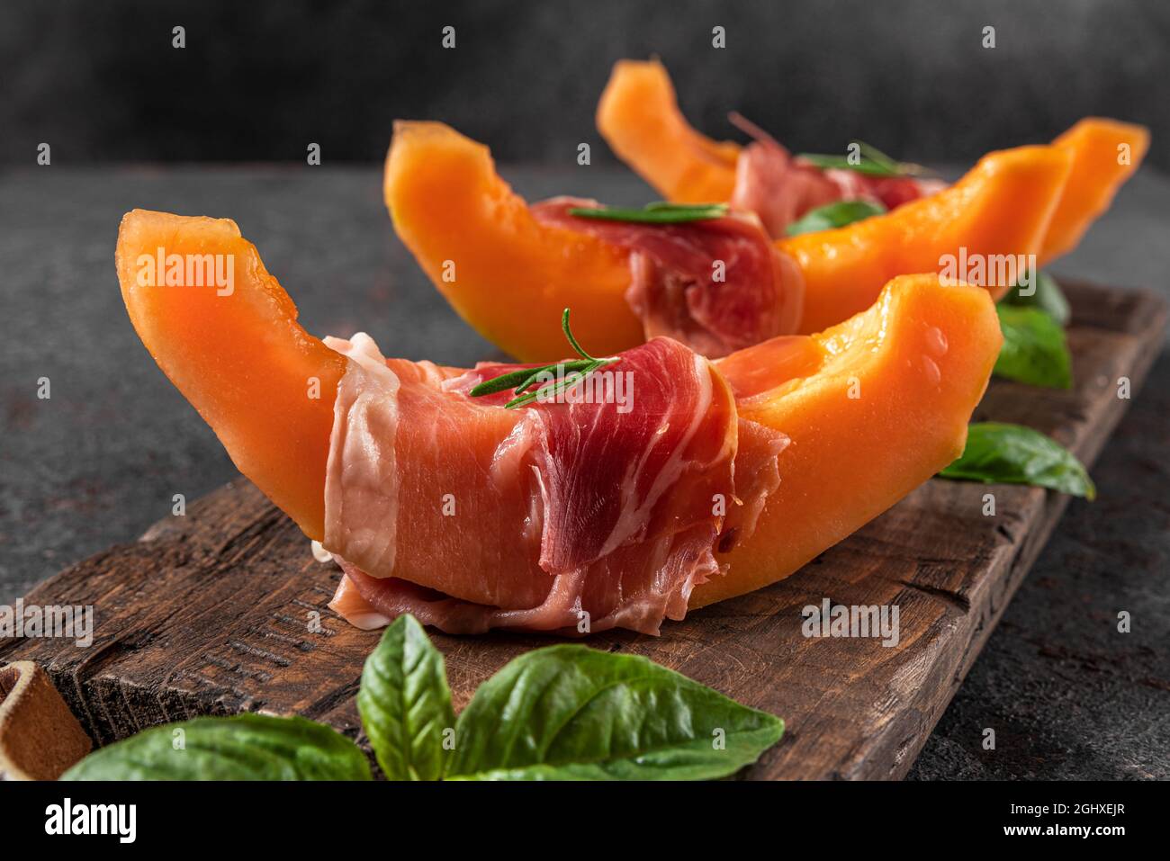 Melone cantalupo fresco con prosciutto e basilico su sfondo nero. Antipasto di cucina italiana. Primo piano Foto Stock