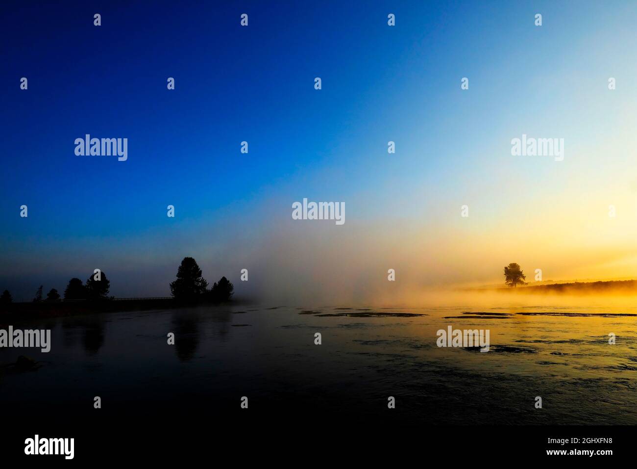 Alba del mattino con alberi e fiume sotto il cielo blu e la nebbia incandescente Foto Stock