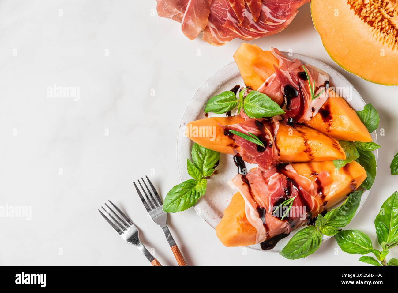 Prosciutto con fette di melone cantalupo, salsa all'aceto balsamico e basilico in un piatto su sfondo bianco. Antipasto italiano. Vista dall'alto con copia sp Foto Stock