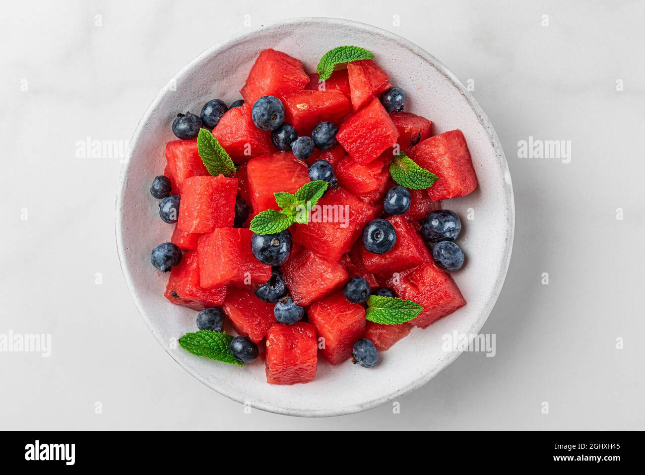 Insalata di melone e mirtillo con menta in un piatto su sfondo bianco. Vista dall'alto. Rinfrescante cibo estivo Foto Stock