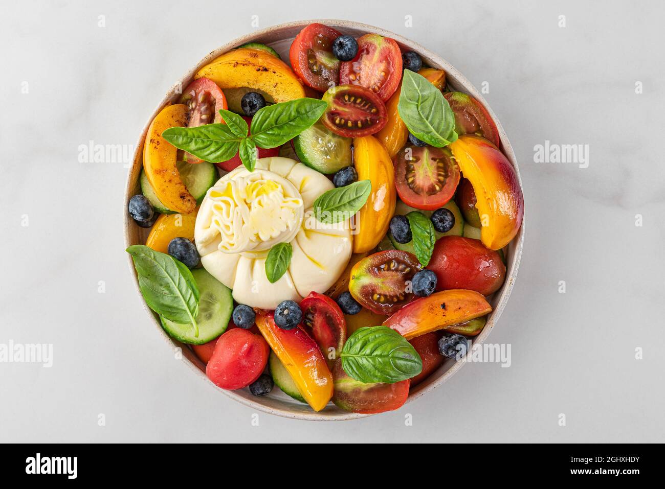 Deliziosa insalata estiva con burrata, pesche alla griglia, pomodori, mirtilli, cetrioli, olio d'oliva e basilico. Vista dall'alto. Dieta sana Foto Stock