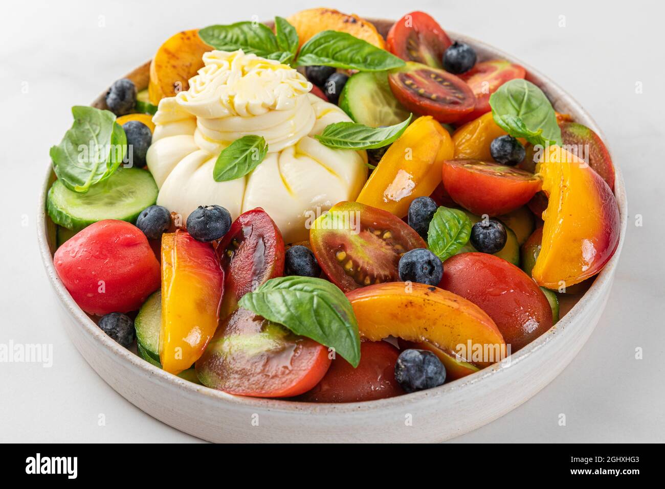 Insalata fresca con pesche alla griglia, burrata, mirtilli, verdure e basilico in un piatto su sfondo bianco. Primo piano. Dieta sana cibo estivo Foto Stock