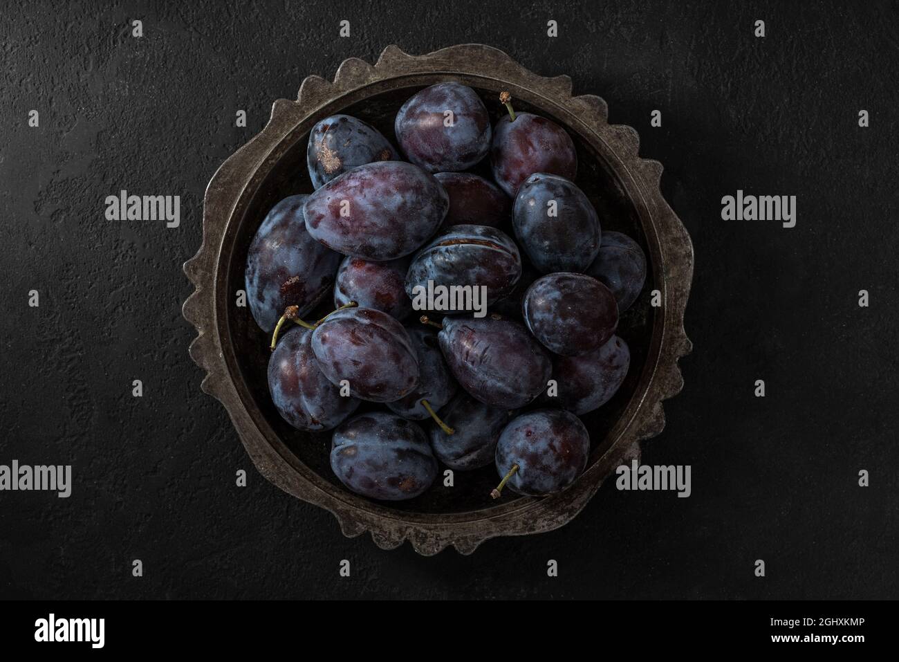 Prugne blu fresche mature in una ciotola su sfondo nero. Vista dall'alto. Tasto basso Foto Stock