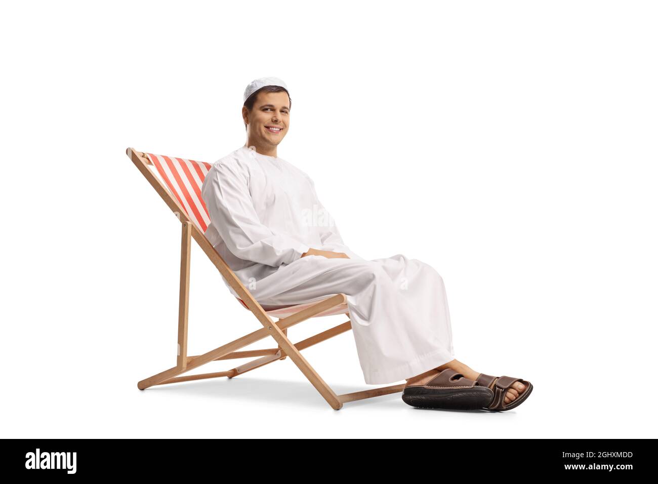 Giovane uomo in abiti etnici seduto su una sedia da spiaggia isolata su sfondo bianco Foto Stock