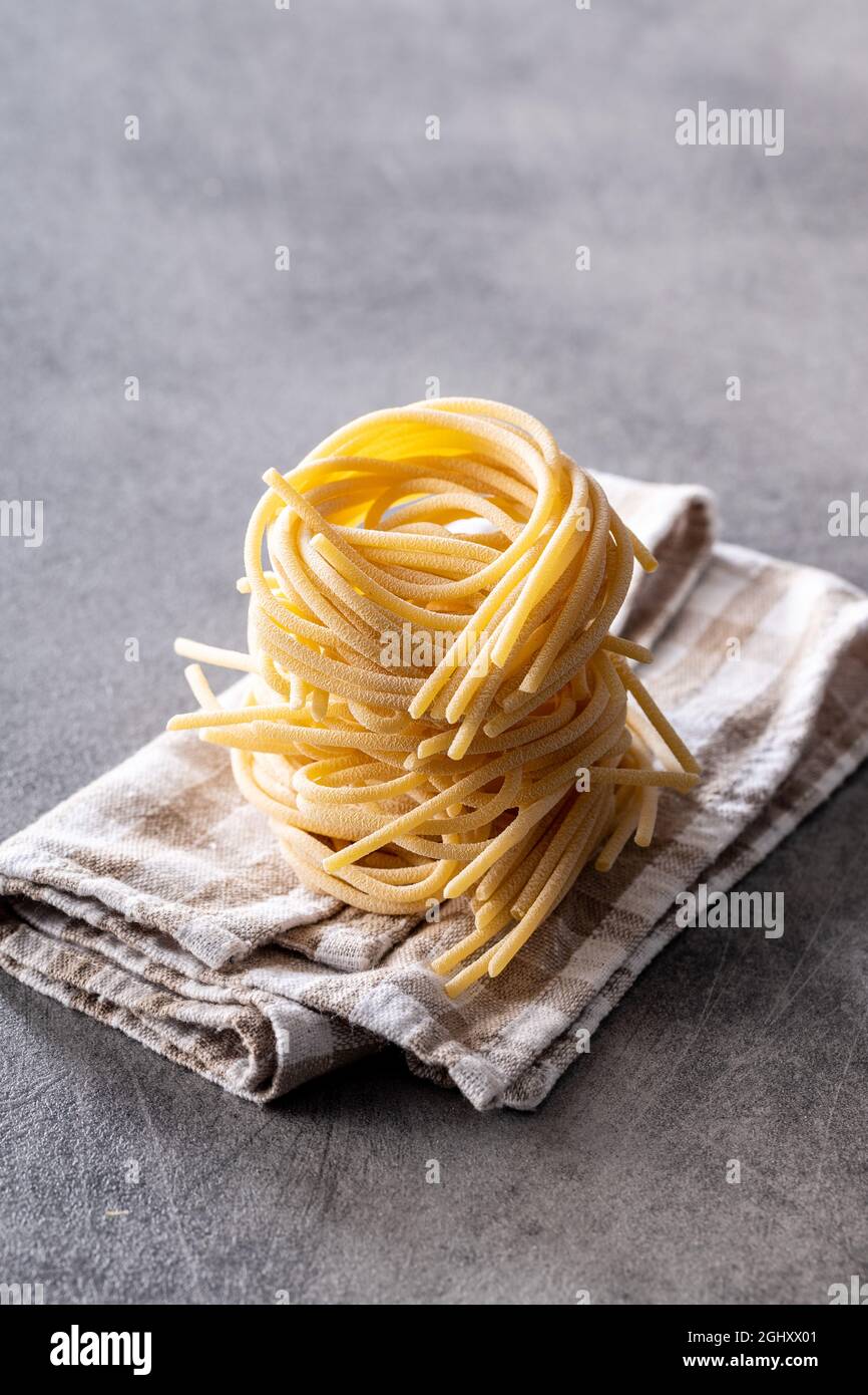 Nido di pasta italiana su tovagliolo. Gli spaghetti non cotti nidificano sul tavolo da cucina. Foto Stock