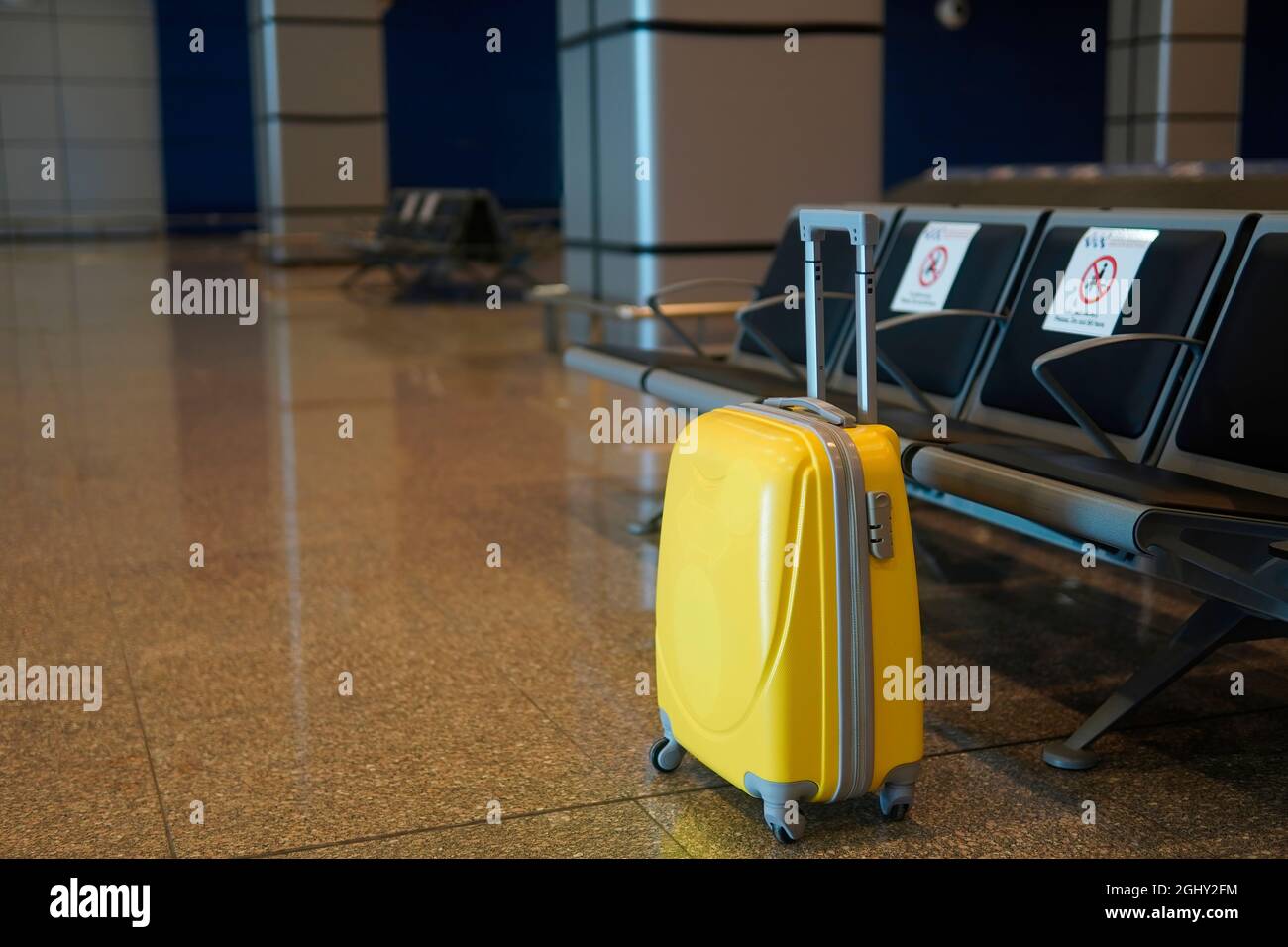 valigia gialla in piedi vicino a posti a sedere vuoti all'aeroporto Foto Stock