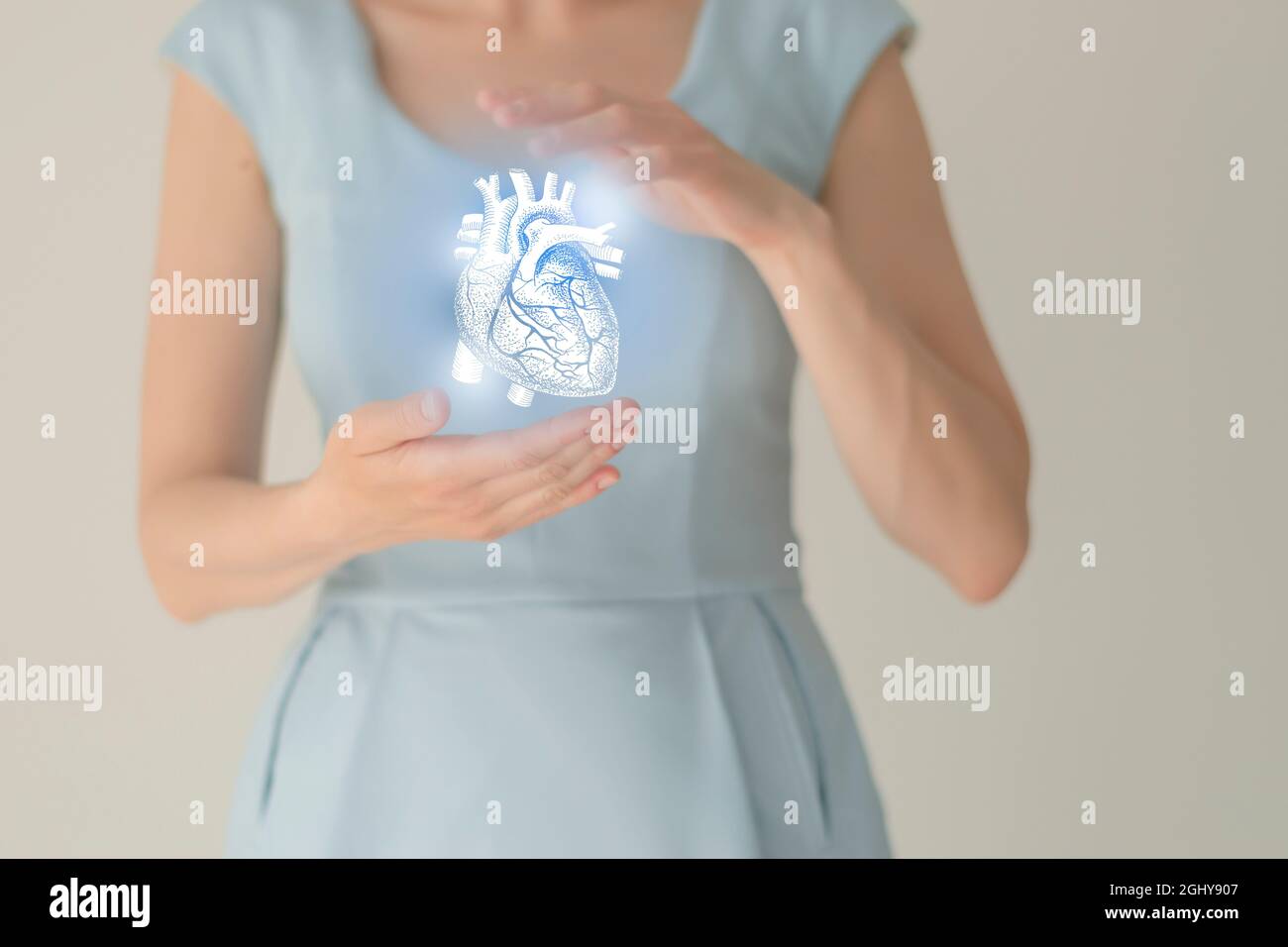 Paziente femminile irriconoscibile in abiti blu, evidenziato cuore di mano nelle mani. Il cuore umano emette il concetto. Foto Stock