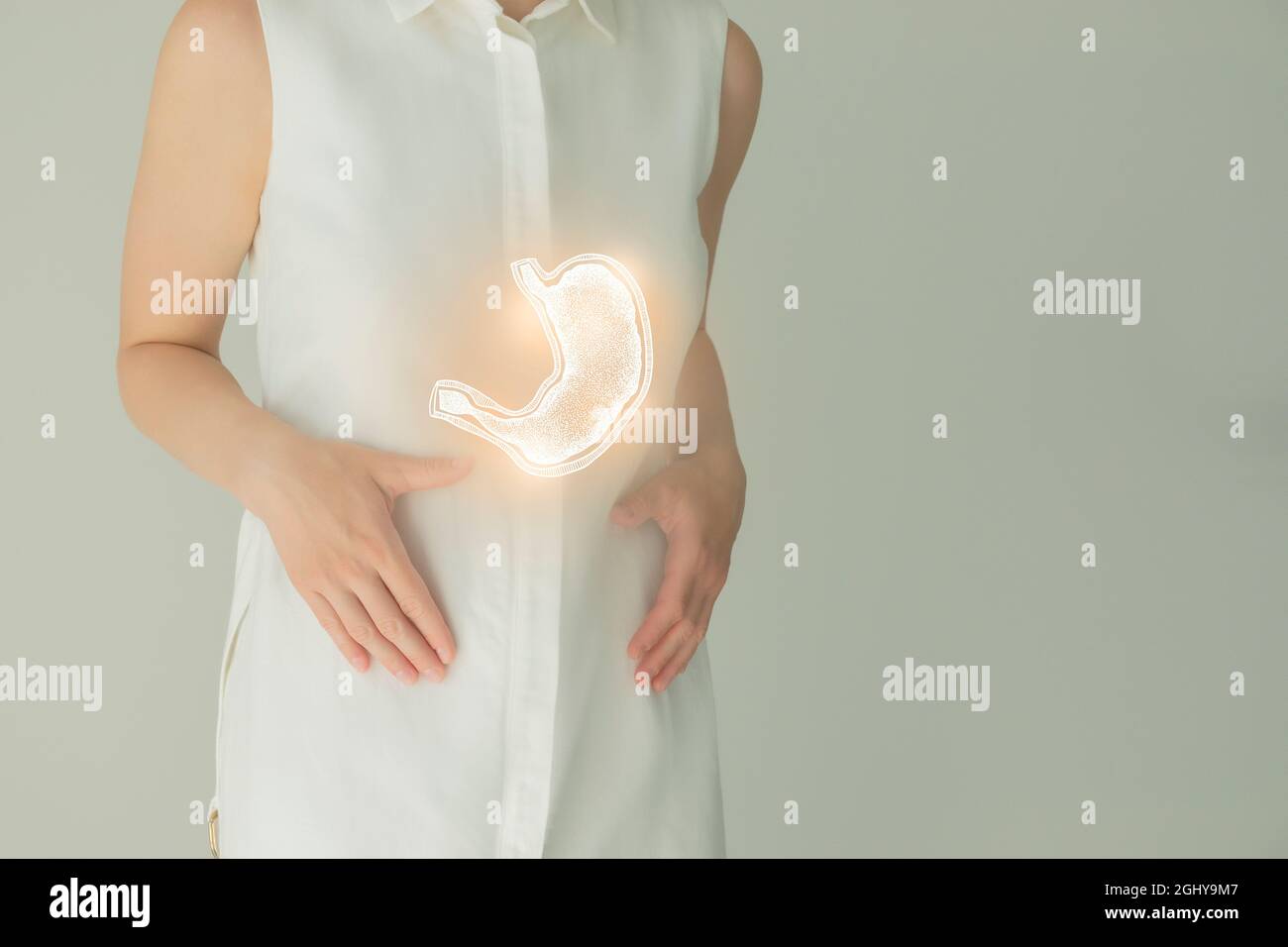 Paziente femminile irriconoscibile in abiti bianchi, evidenziato stomaco di mano nelle mani. Concetto di problemi del sistema digestivo umano. Foto Stock