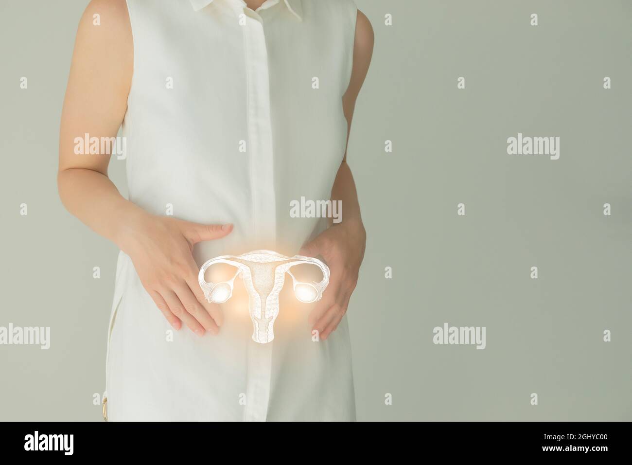 Paziente femminile irriconoscibile in abiti bianchi, evidenziato utero di mano nelle mani. Concetto di problemi del sistema riproduttivo umano. Foto Stock