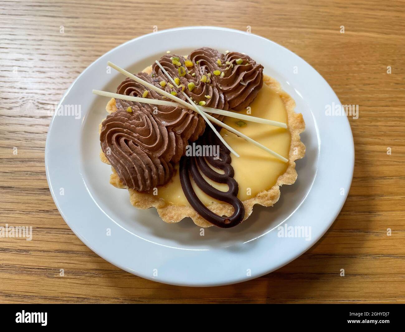 Delizioso tartetto con budino e panna montata parigina servita su un piatto bianco su un tavolo di legno Foto Stock