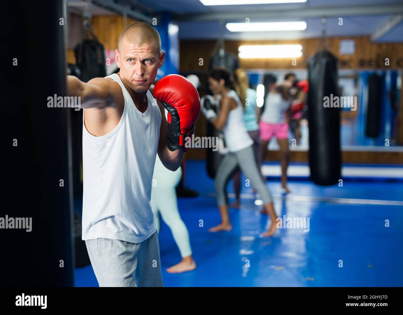 Giovane uomo in guanti da boxe che pratica punzoni su borsa in palestra Foto Stock