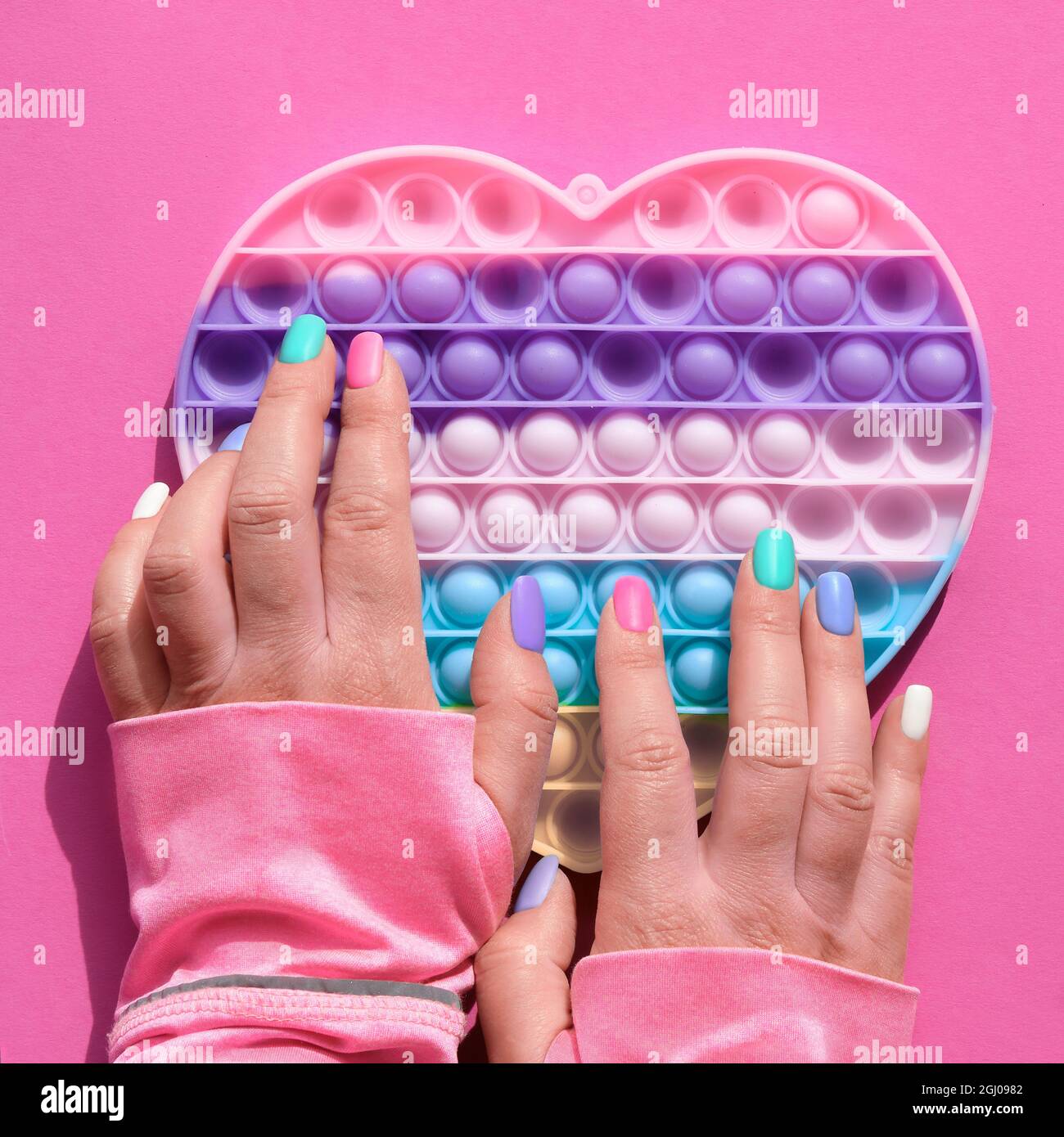 Cuore a forma di papa esso antistress giocattolo con mano femminile. Semplice fodget sensoriale a concavità nei colori di LGBT. Piatto posare su carta rosa, composizione quadrata. Aiuto Foto Stock