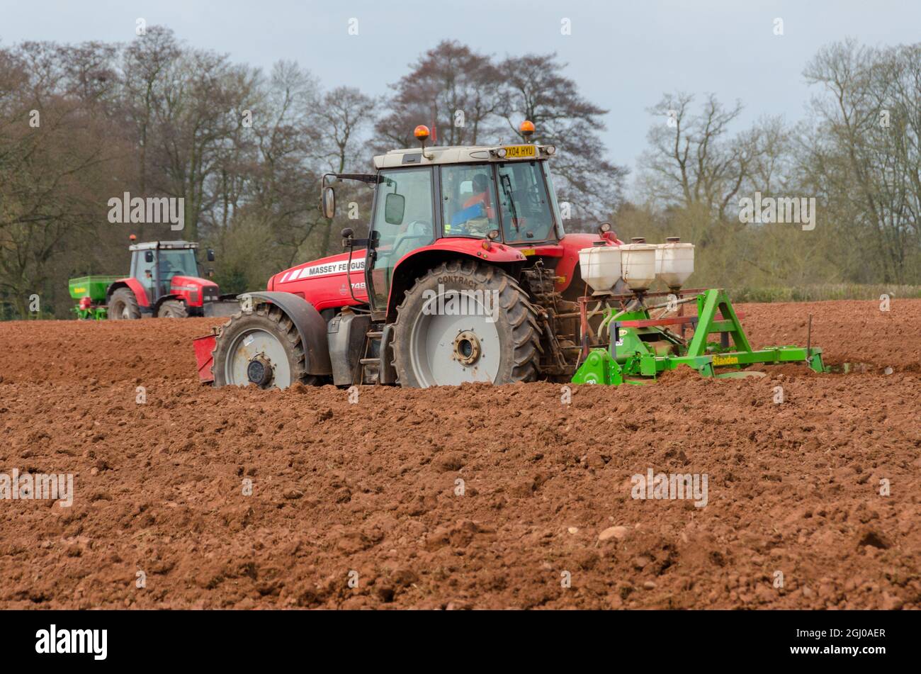 Due trattori Massey Ferguson rossi che seminano semi in un campo arato Foto Stock