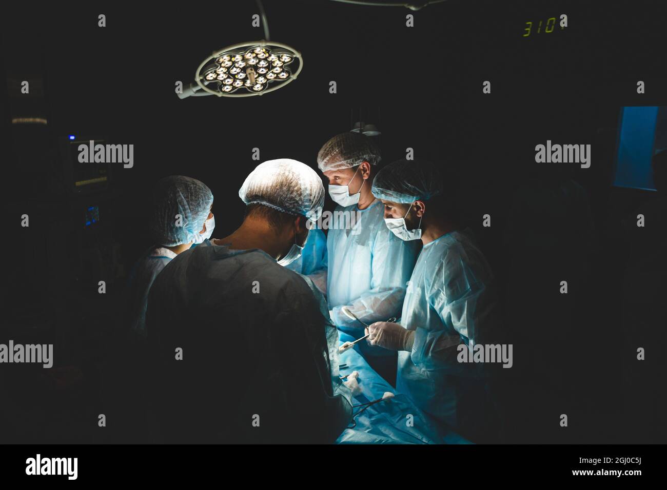 Un team professionale internazionale di chirurgo, assistenti e anestesista esegue un'operazione complessa su un paziente sottoposto ad anestesia generale. Scuro Foto Stock