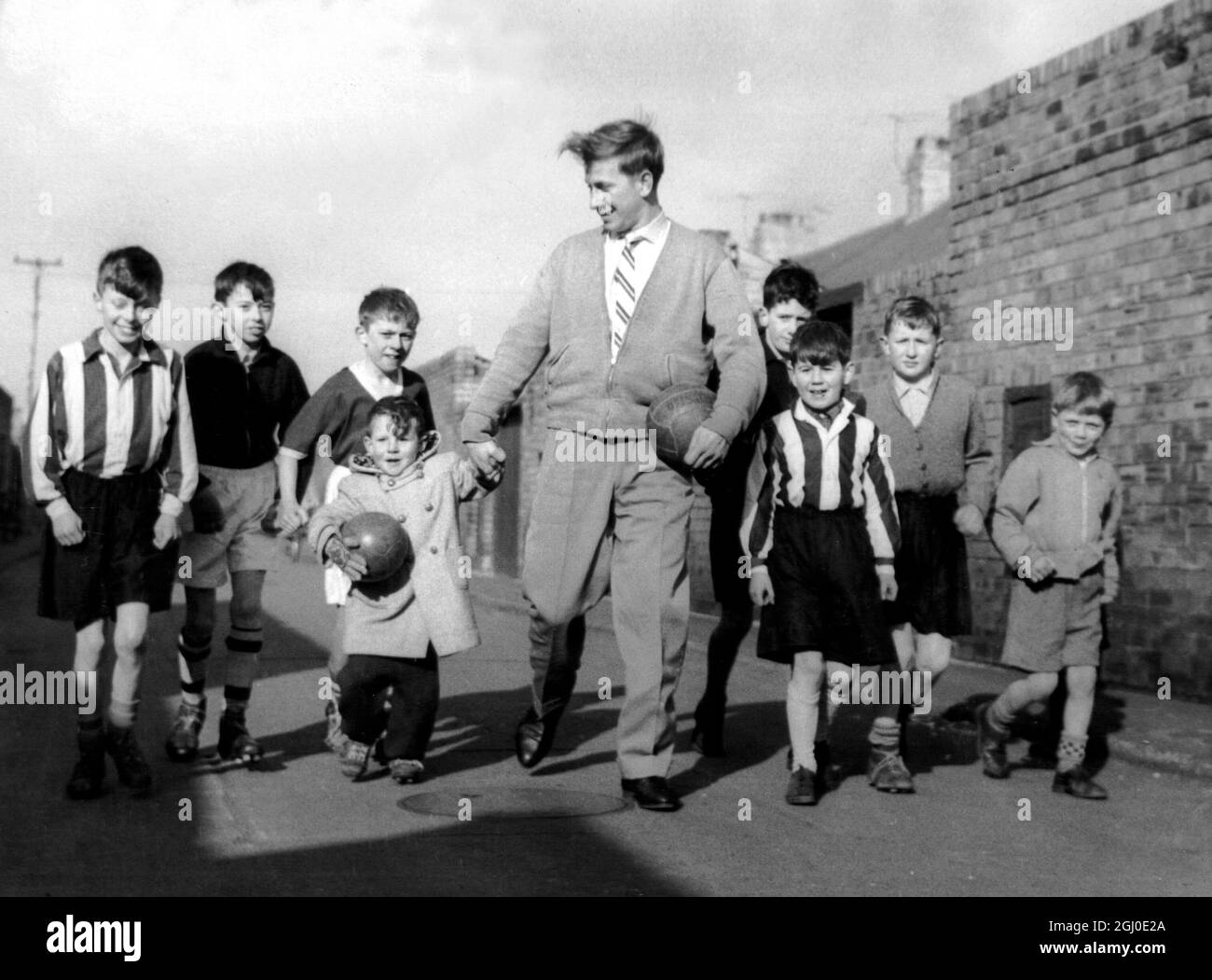 Bobby Charlton di Manchester Utd, con alcuni dei bambini locali, calcia una palla nella corsia posteriore della sua casa a Beatrice Street, Ashington, Northumberland. Foto Stock Bobby Charlton di Manchester Utd, con alcuni dei bambini locali, calcia una palla nella corsia posteriore della sua casa a Beatrice Street, Ashington, Northumberland. Foto Stock