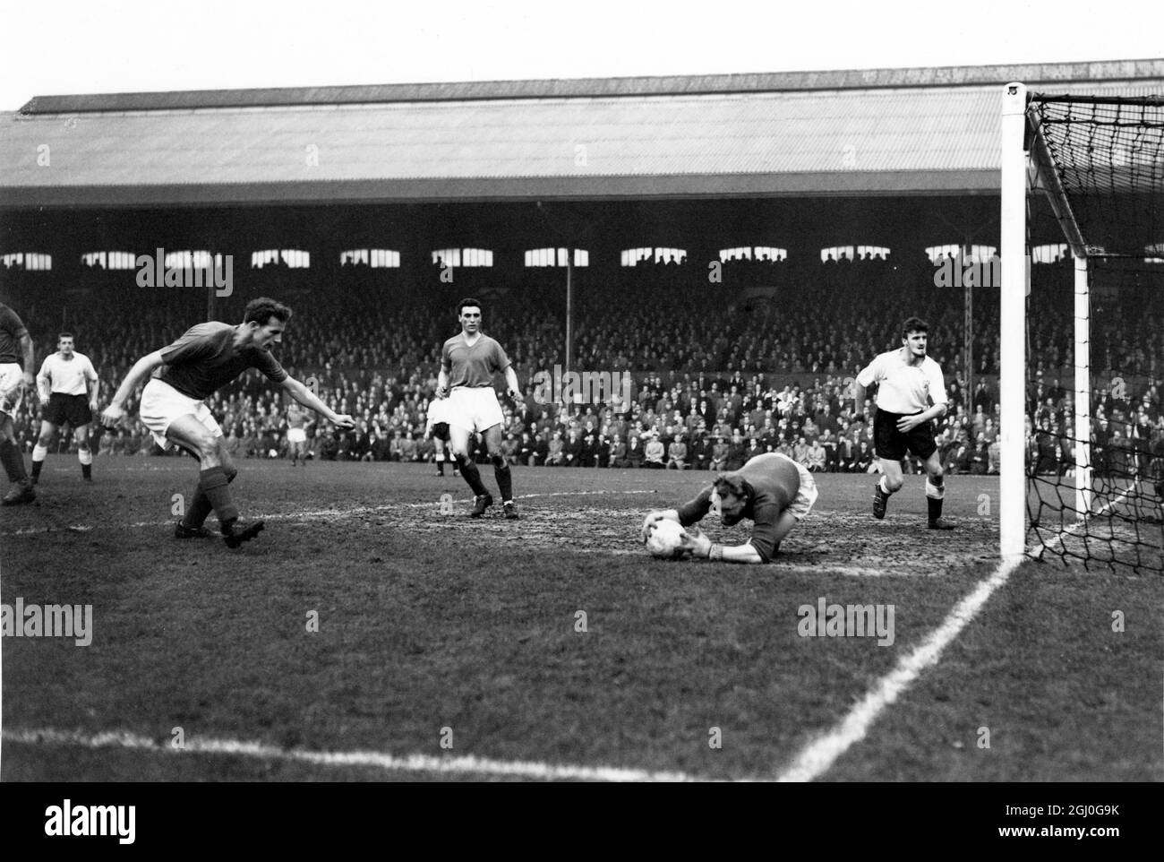 Barnsley v Fulham Barnsley portiere Hough, si tuffa per abbracciare la palla, come egli salva da una squadra Fulham attaccante, durante il gioco a Craven Cottage. Nella bocca del palco c'è Fulham dentro a destra, Jimmy Hill. 29 novembre 1958 Foto Stock