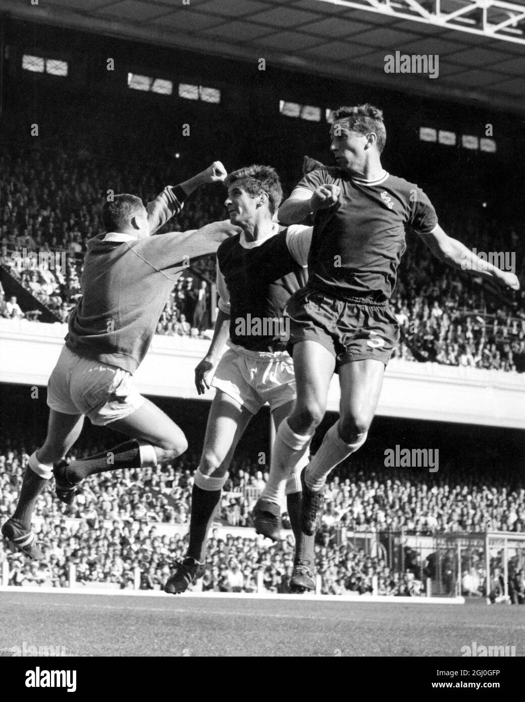 Arsenal contro Chelsea eccitamento intorno al gol-bocca dell'Arsenal come loro portiere, Jim Furnell punches libera una sfera dall'ala. Center-Half, Gordon Ferry (in sostituzione di Ian Ure) tiene la guardia della metà destra del Chelsea, John Hollins, durante il Derby di Londra Ay Highbury. 26 settembre 1964 Foto Stock