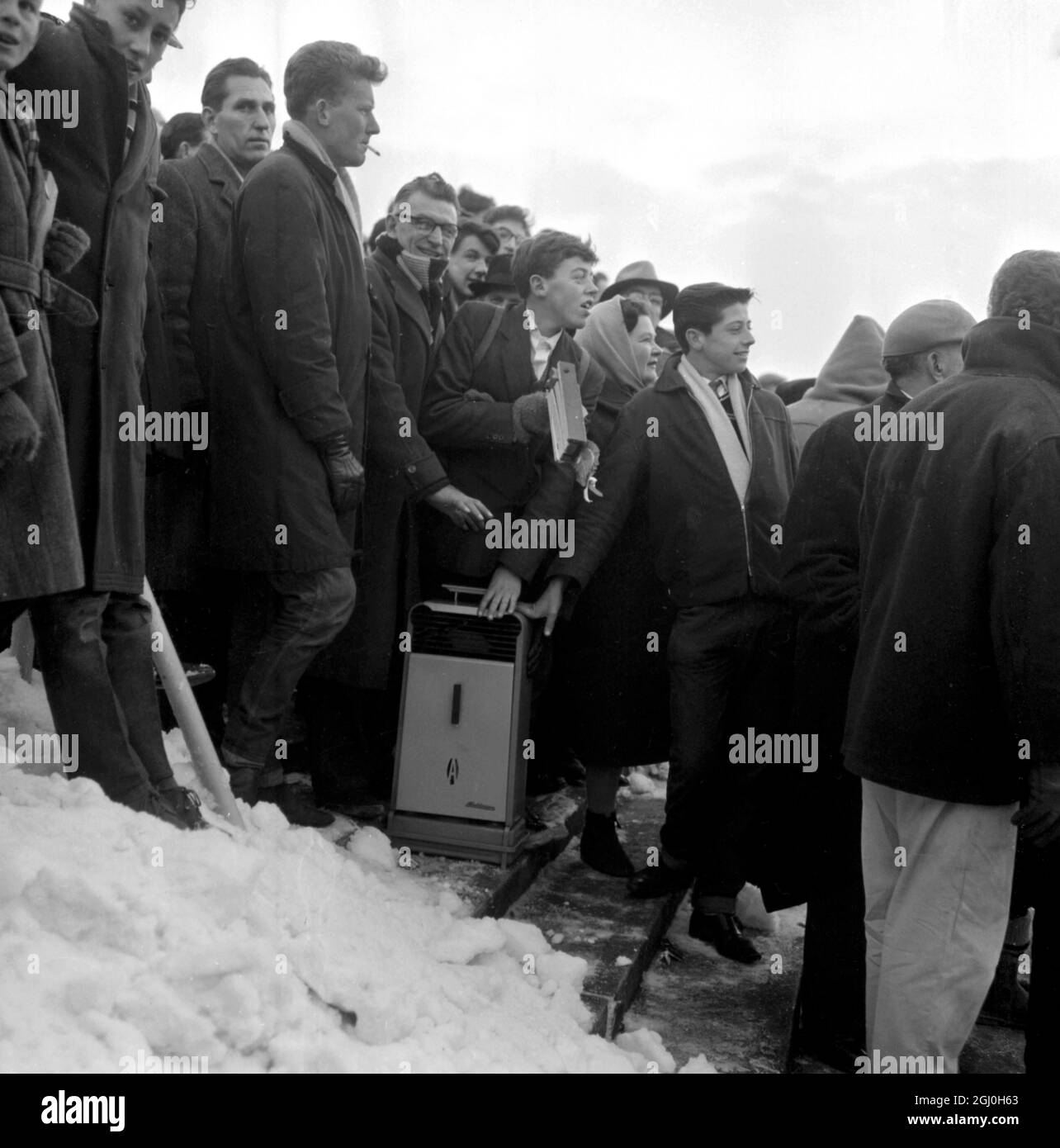 Brighton, Inghilterra: Questi tifosi di Brighton hanno preso un riscaldatore dell'olio per caldarsi tra la neve mentre guardavano il Palazzo di Cristallo di Brighton V. Brighton ha perso 1 - 2. 12 gennaio 1963 Foto Stock