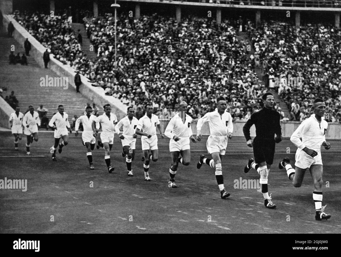 Olimpiadi del 1936, Berlino - la squadra nazionale tedesca di pallamano si disputerà alle urla dei centomila spettatori attorno al campo olimpico per la partita finale. (Die deutsche Handball-Nationalmannschaft sturmt unter dem Jubel der Hunderttausend in die olympische Kampfbahn zum Endspiel.) La squadra tedesca è composta da: Karl Kreutzberg, Arthur Knautz, Willi Bandholz, Hans Keiter, Wilhelm Brinkmann, Rudolf Stahl, Fritz Spengler, Erich Hermann, Günter Ortmann, Wilhelm Baumann, Fritz Fromm, Heinz Körvers, Wilhel Muller, Georg Dascher, Kurt Dossin, Hermann Hansen, Edgar Reinhardt, Hans Theilig, Helmut BE Foto Stock