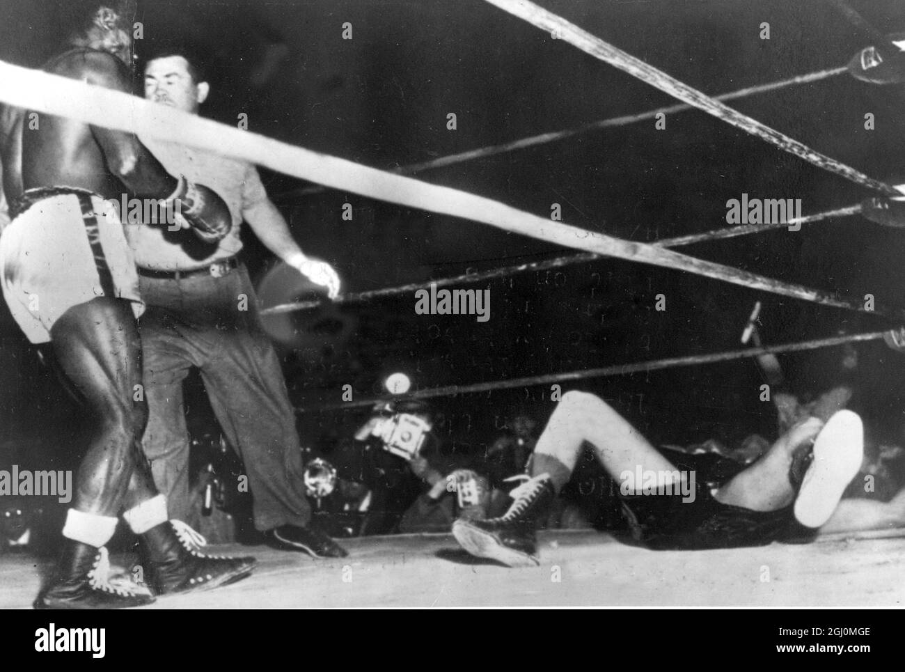 Wrigley Field , Los Angeles . Hogan ' Kid ' Bassey della Nigeria il campione del mondo dei pesi piuma è trattenuto dall'arbitro dopo che l'ex aveva galleggiato Ricardo ' Little Bird ' di Liverpool nel terzo round . Il conteggio è terminato con solo secondi del giro per andare . 3 aprile 1958 Foto Stock