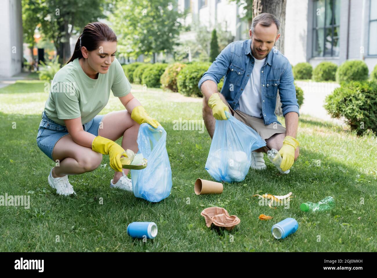 Coppia sorridente in guanti di gomma raccolta rifiuti in borse sul prato Foto stock Alamy