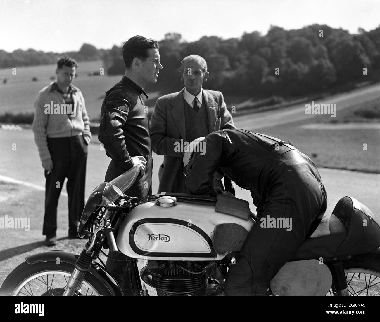 Geoff Duke , (senza casco ) campione britannico di motociclette da corsa su strada, si rilassa e parla con un altro concorrente durante la pratica al Brands Hatch Racing Curcuit nel Kent . 24 settembre 1955 Foto Stock