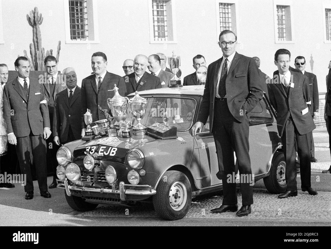 Monte Carlo , Monaco : il cofano del Morris Cooper S coperto di trofei , Paddy Hopkirk britannico (quarto da sinistra) e il co-driver Henry Liddon (primo piano) sono raffigurati dopo la presentazione dei trofei qui 25 gennaio 1964 , alla fine del Montre carlo Rally 1964 . Paddy è il primo pilota britannico a vincere il rally dal 1956. La British Motor Corporation ( BMC ) ha vinto il premio costruttori il 27 gennaio 1964 Foto Stock