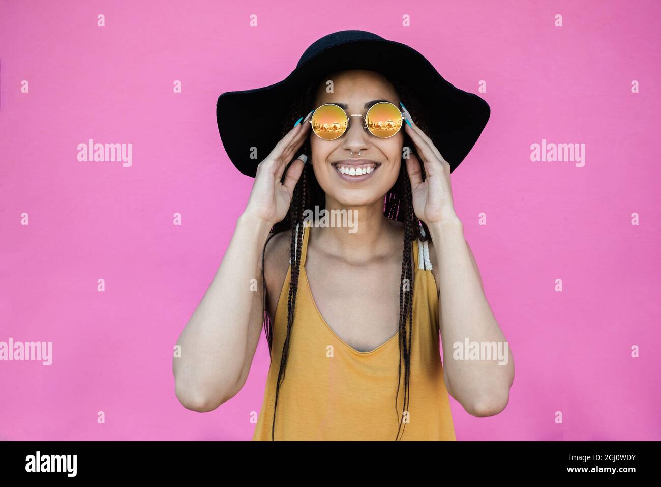 Ragazza africana hipster sorridente alla macchina fotografica all'aperto con sfondo rosa - fuoco sul volto Foto Stock