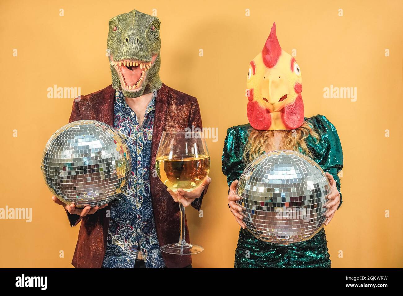 Coppia pazza divertirsi festeggiando la festa di Capodanno con palle da discoteca e bicchiere di vino - Focus su t-rex e maschera di pollo Foto Stock