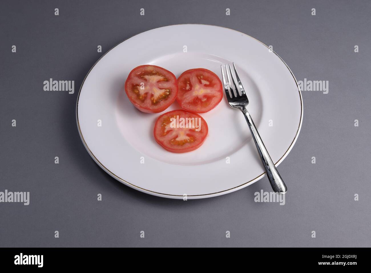 un pomodoro affettato su un piatto di porcellana bianca con una forchetta Foto Stock
