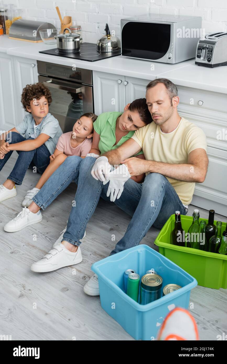 Famiglia stanca seduta sul pavimento vicino spazzatura in scatole a casa Foto Stock