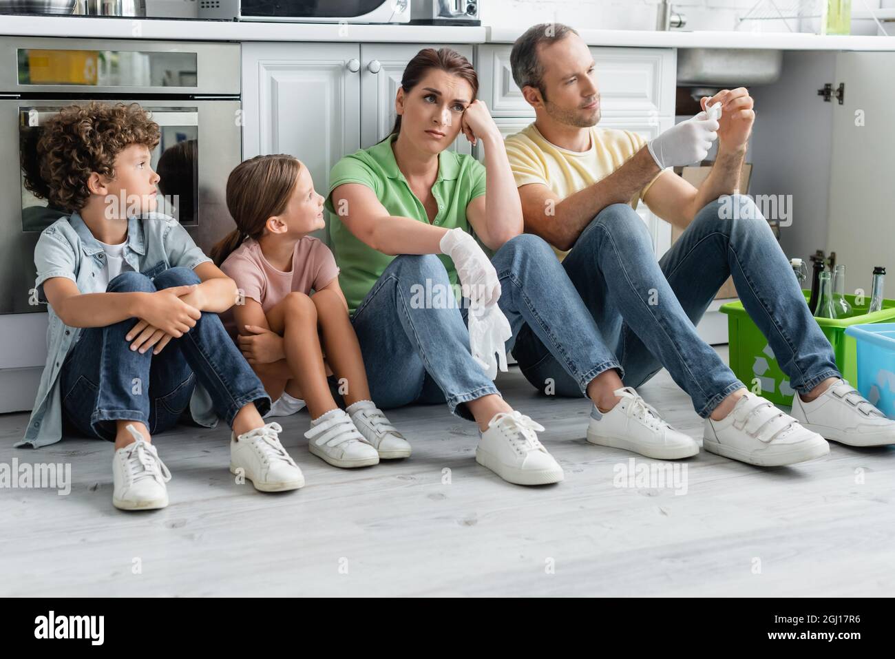 Famiglia esausta con bambini seduti vicino a scatole con segno di riciclaggio in cucina Foto Stock