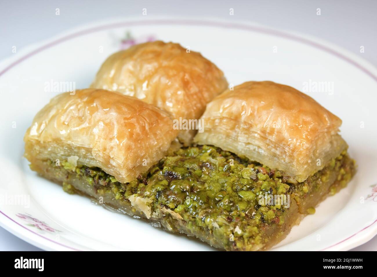Delizioso primo piano pistacchio baklava su un piatto bianco. Uno di loro è stato tagliato a metà per mostrare i suoi pistacchi. Foto Stock