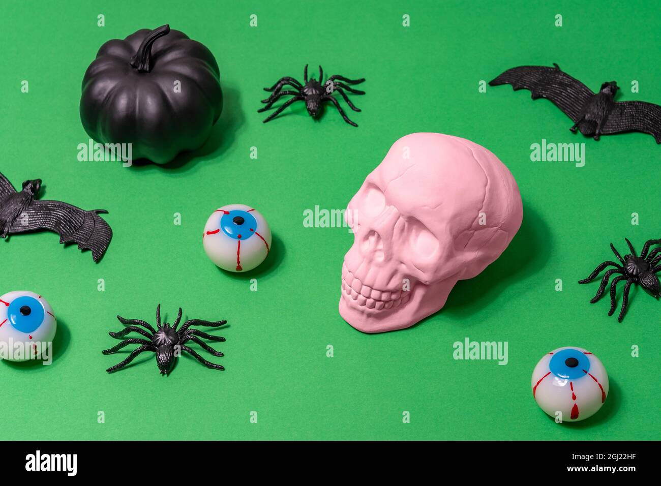 Layout di Halloween con cranio rosa, ragni, pipistrelli e sopracciglia su sfondo verde. Minimo concetto di vacanza. Foto Stock