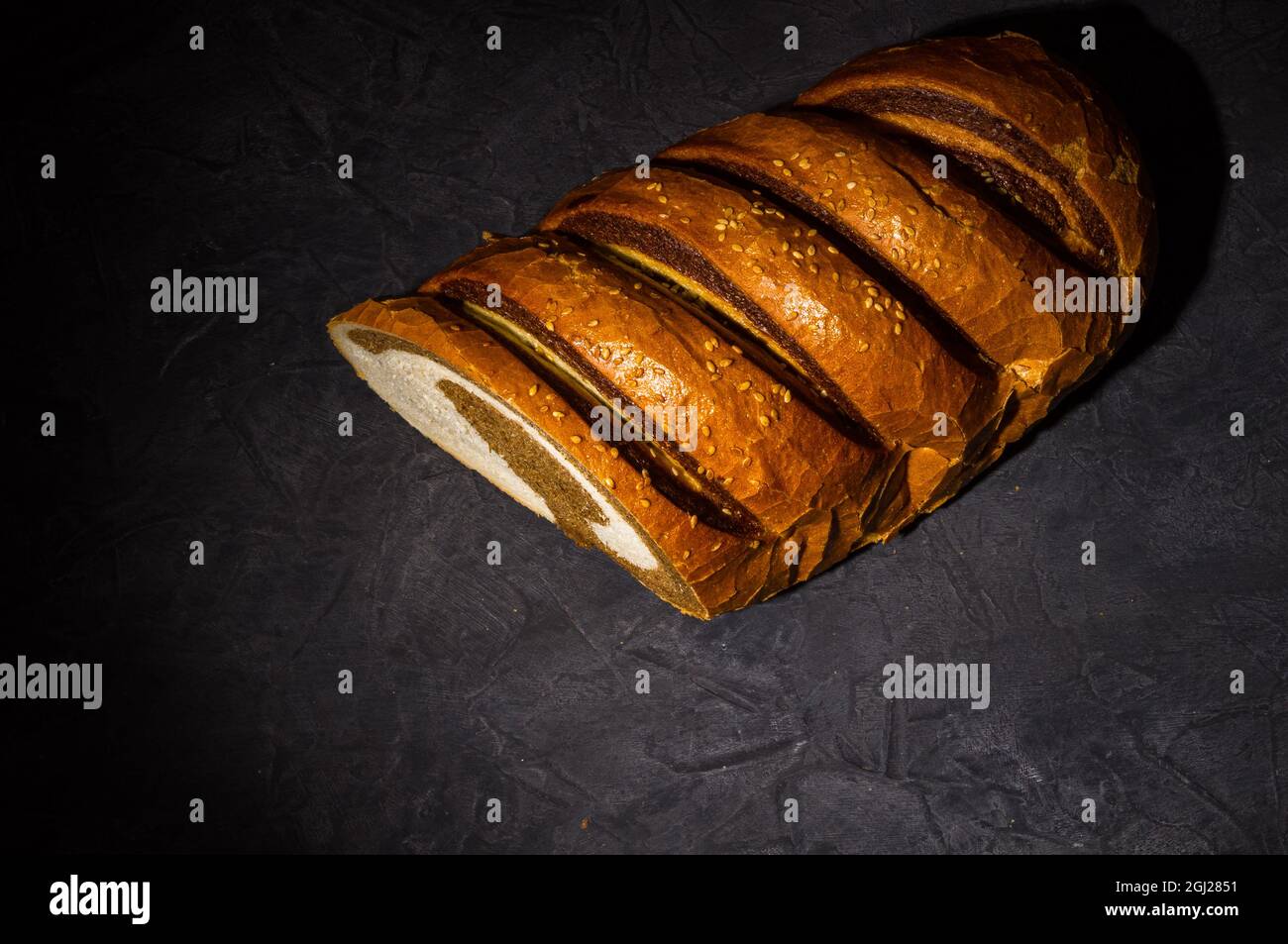 Insolita pagnotta di pane fresco a due colori su sfondo nero, foto in un tasto basso in luce dura, primo piano. Foto Stock