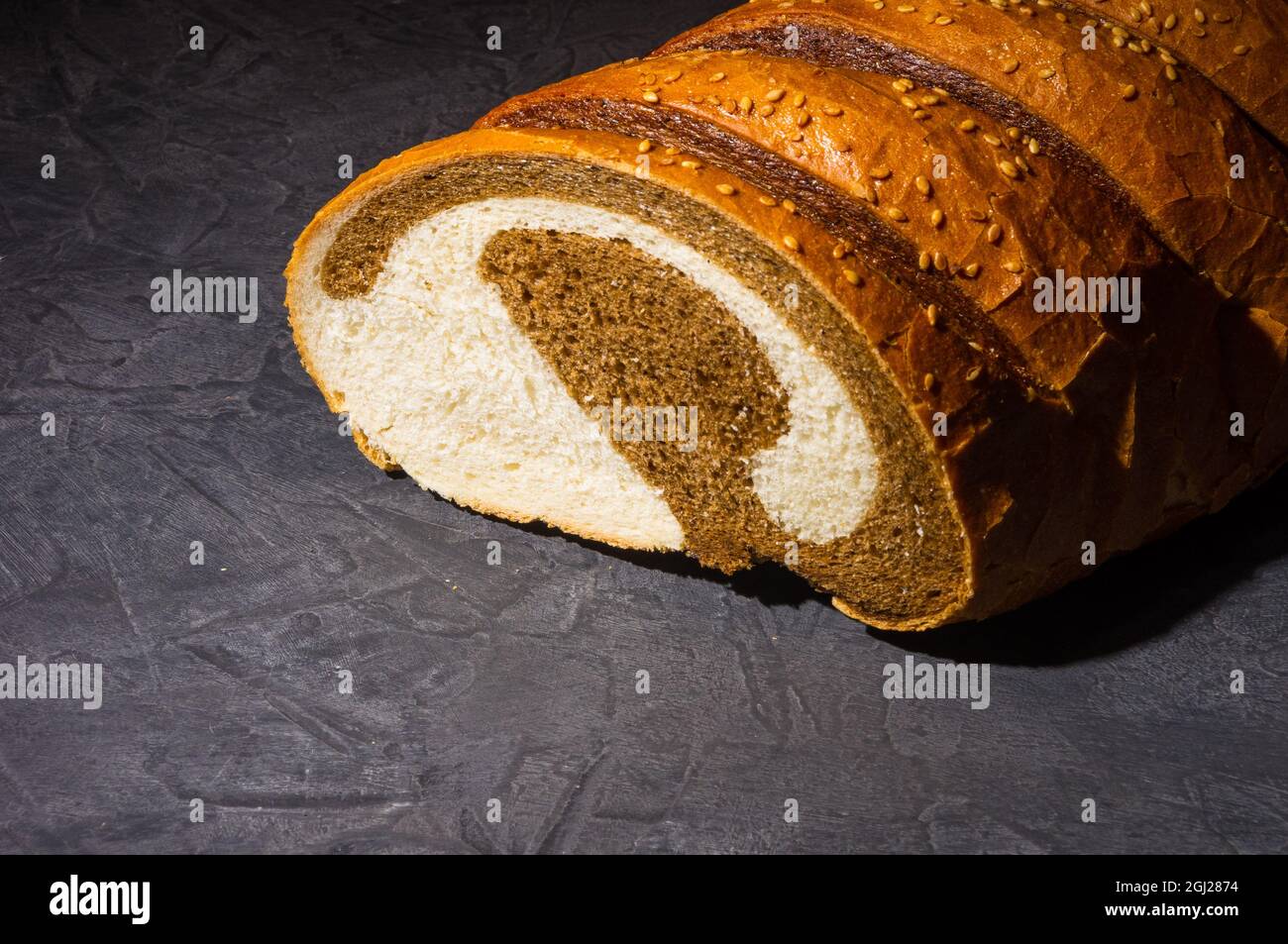 Insolita pagnotta di pane fresco a due colori su sfondo nero, foto in un tasto basso in luce dura, primo piano. Foto Stock