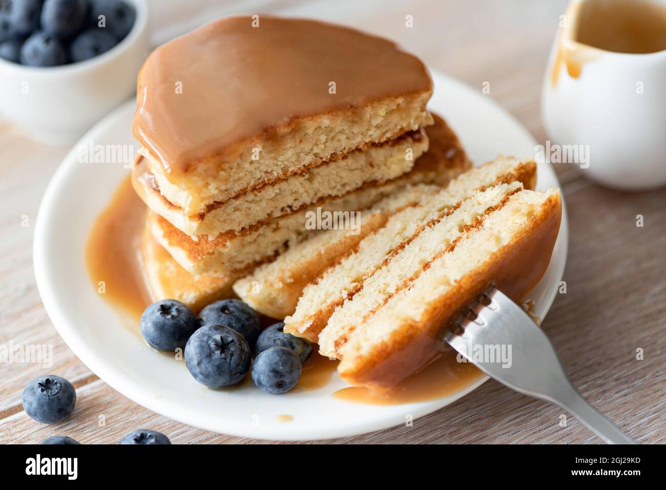 Tagliare la pila di pancake con salsa al caramello e mirtilli sul piatto Foto Stock
