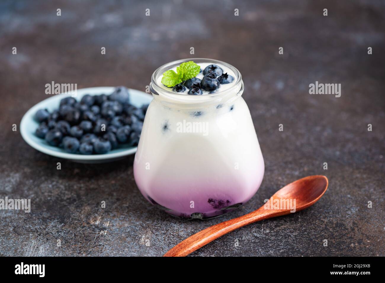 Yogurt al mirtillo in vaso su fondo tavola di cemento. Cibo sano, snack fitness dolce Foto Stock