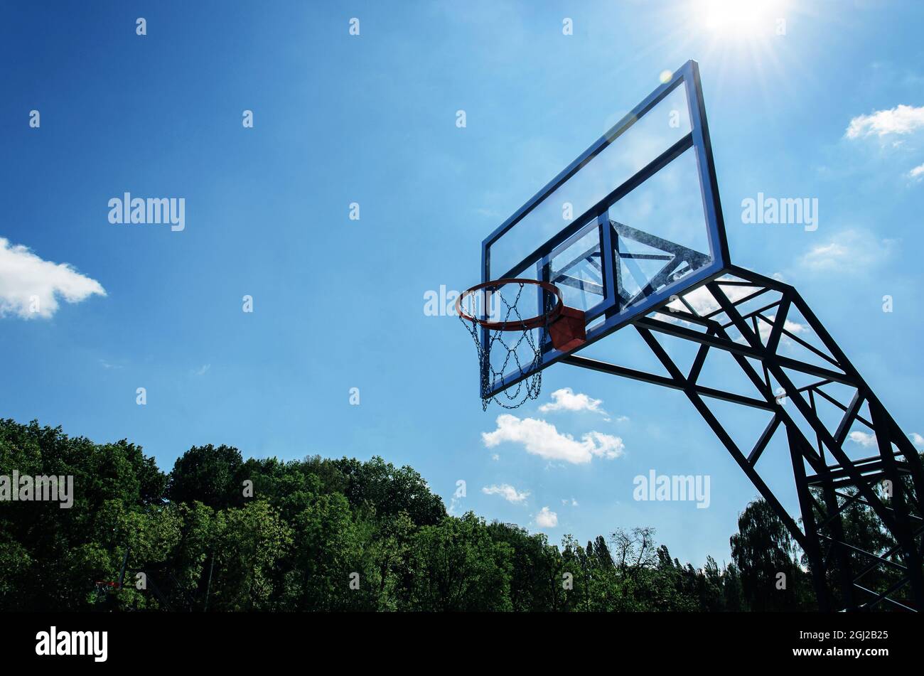 Canestro da basket e backboard in vetro trasparente contro il cielo blu nel parco cittadino nelle giornate di sole. Attrezzature per gli sport di strada a terra. Spazio di copia Foto Stock