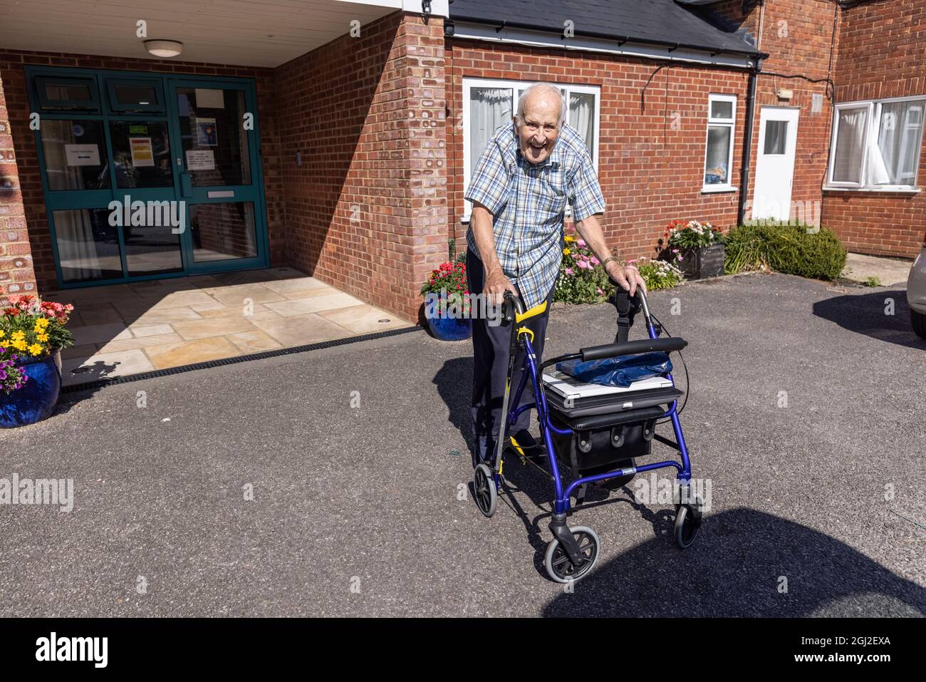Un uomo anziano che cammina con un 'Glider Rollator' fuori da una casa di cura in Hampshire, Inghilterra, Regno Unito Foto Stock