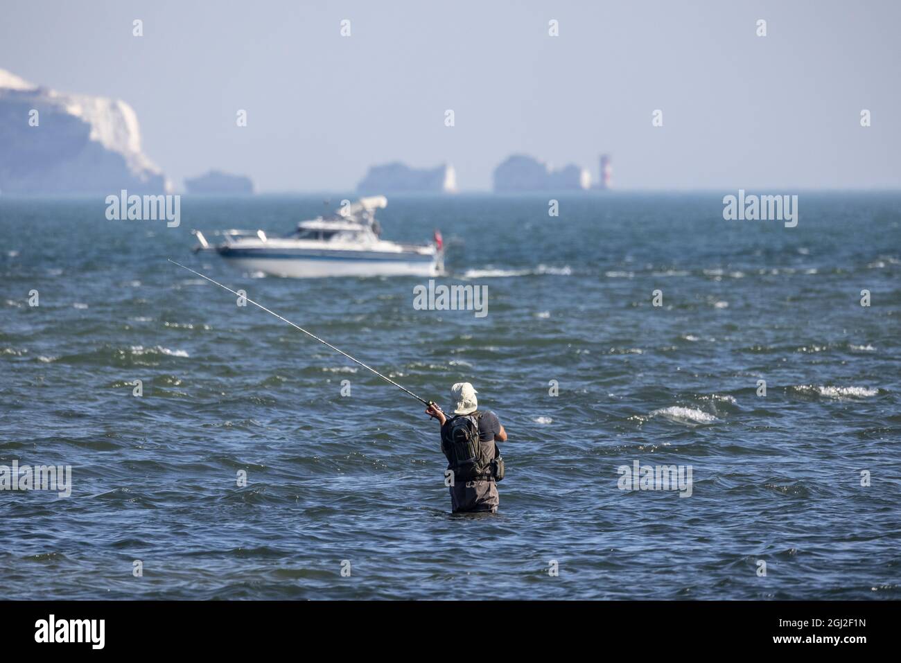 Un pescatore in waders getta la sua linea fuori nel solent poco profondo tratto di acqua di marea con Isle of Weight in Distance, Hampshire e Dorset costa. Foto Stock