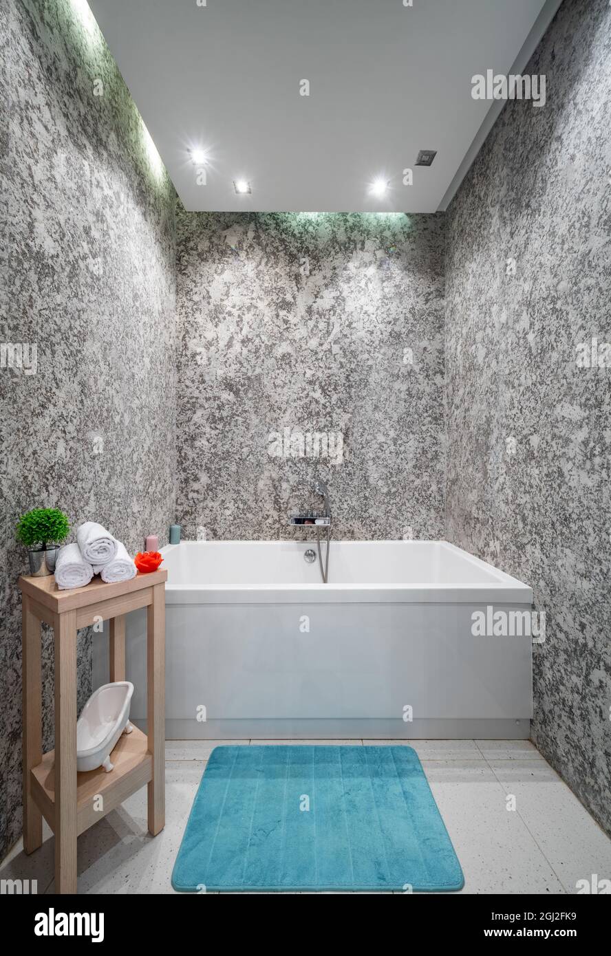 Moderno bagno interno in appartamento di lusso. Pareti in granito. Vasca da  bagno. Sgabello in legno con asciugamani bianchi. Tappeto turchese Foto  stock - Alamy