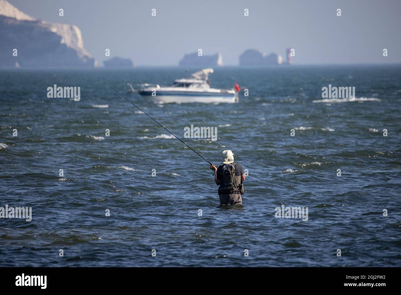 Un pescatore in waders getta la sua linea fuori nel solent poco profondo tratto di acqua di marea con Isle of Weight in Distance, Hampshire e Dorset costa. Foto Stock