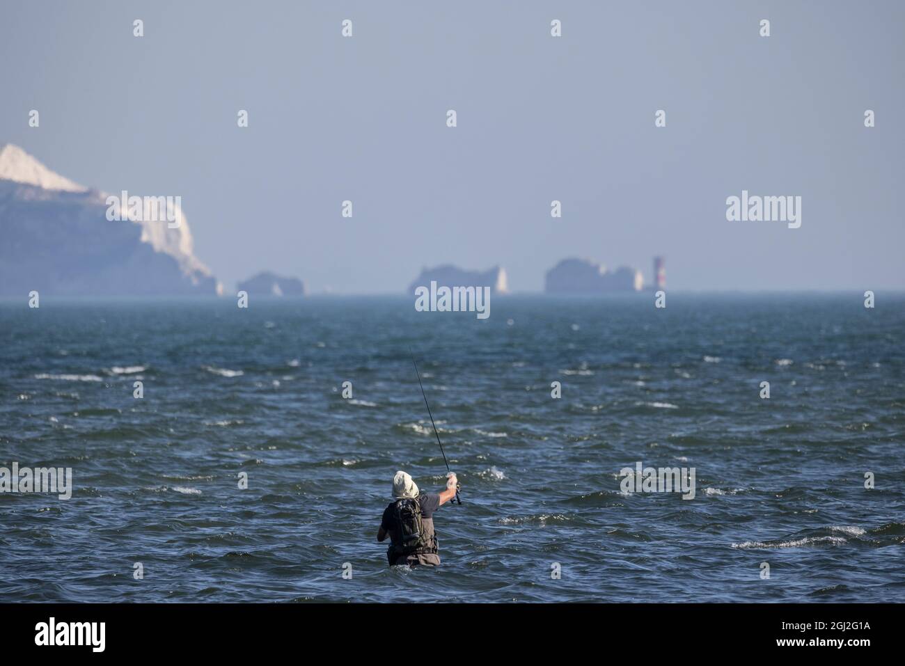 Un pescatore in waders getta la sua linea fuori nel solent poco profondo tratto di acqua di marea con Isle of Weight in Distance, Hampshire e Dorset costa. Foto Stock