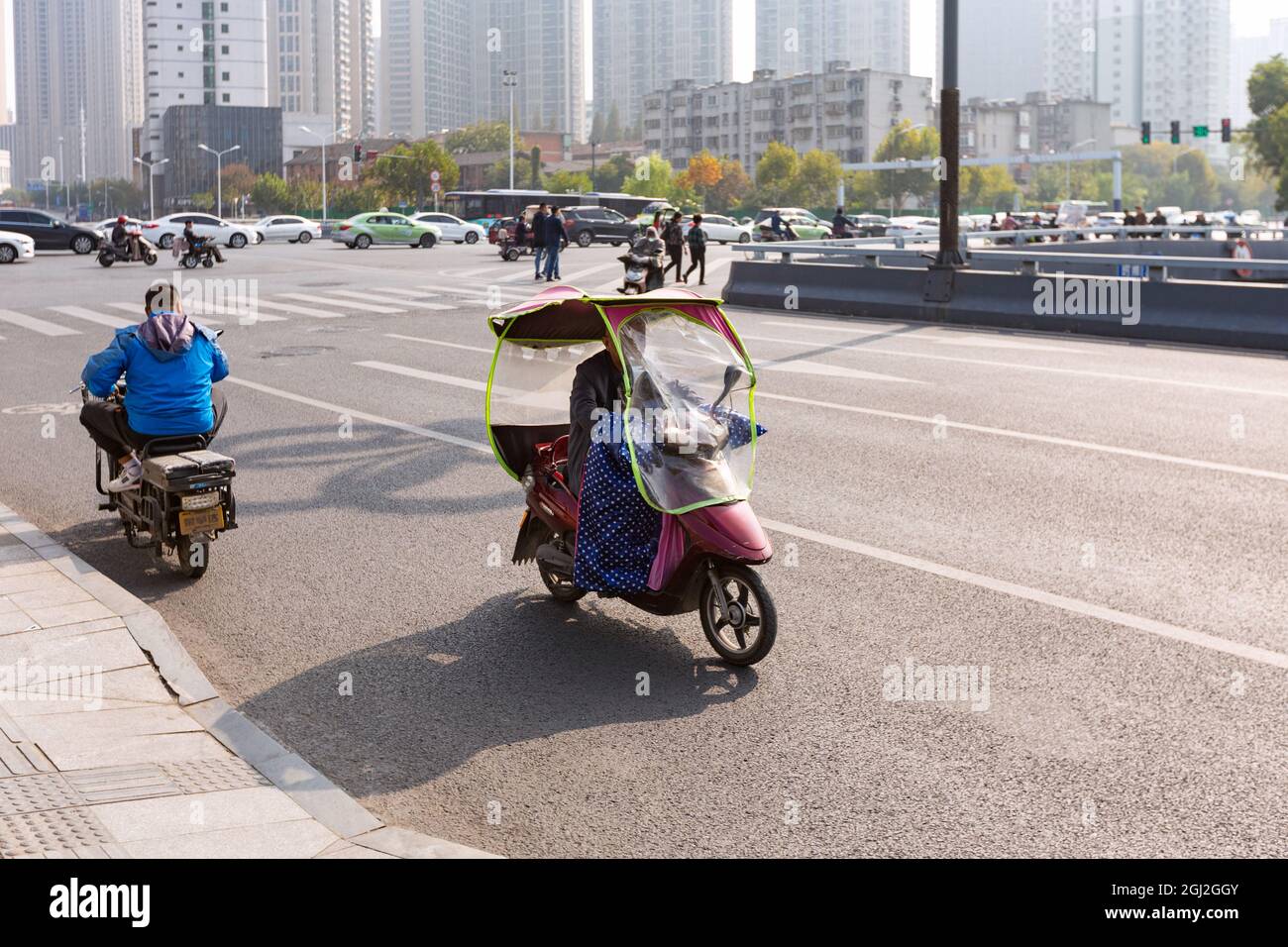 Persone in bicicletta elettrica con parabrezza colorato sull'incrocio, Hefei, Cina. Foto Stock