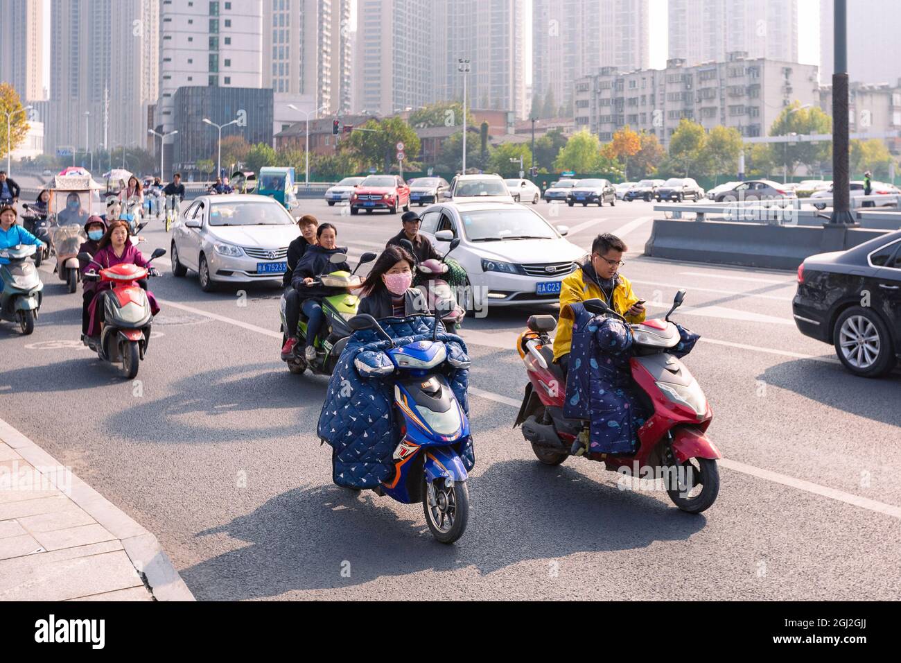 Persone in bicicletta elettrica con parabrezza colorato sull'incrocio, Hefei, Cina. Foto Stock
