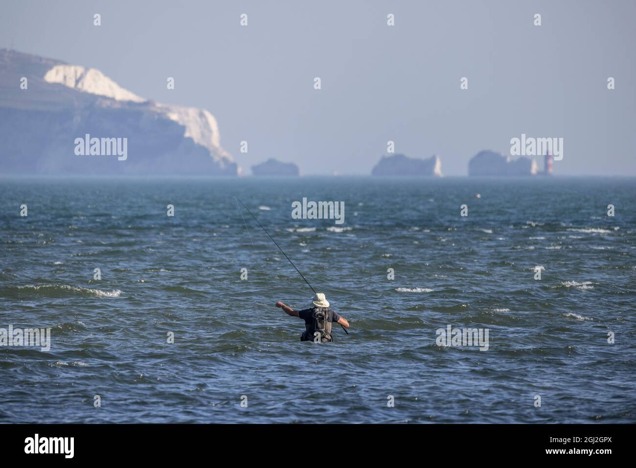 Un pescatore in waders getta la sua linea fuori nel solent poco profondo tratto di acqua di marea con Isle of Weight in Distance, Hampshire e Dorset costa. Foto Stock