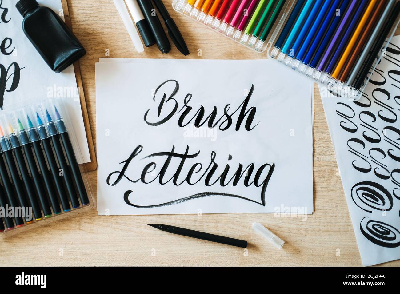 Pennello testo letterato su carta e pennelli e matite colorate sulla tabella. Lettere arte e calligrafia. Testo scritto a mano Pennello le lettere su bianco Foto Stock