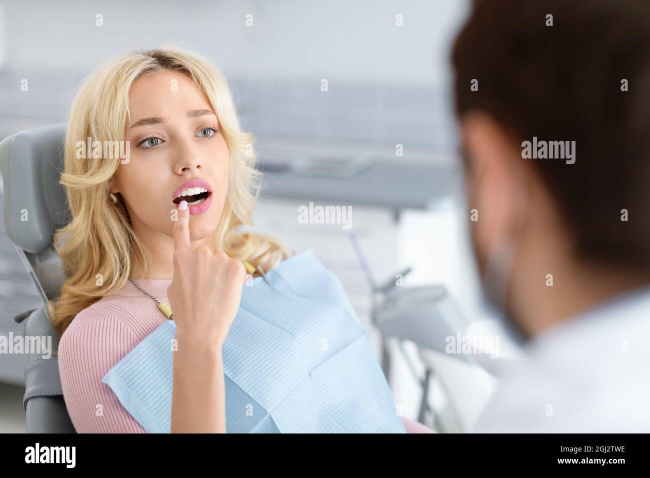 Attraente giovane donna bionda visita clinica dentale, seduta sulla sedia dentale, indicando il dente irritante, sofferente di dolore, avendo conversazione Foto Stock